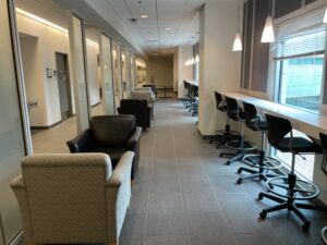 line of armchairs facing each other on the left, and bar stool seating at a bar looking out windows on the right